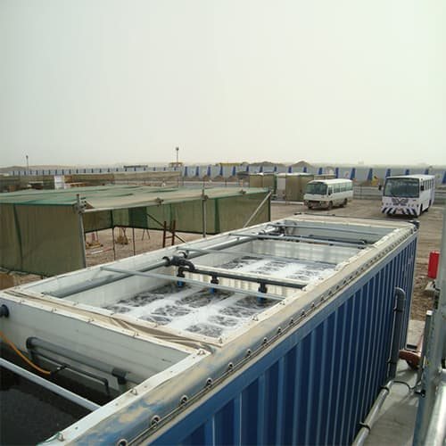 BioKube container plant with open-top aeration tanks in operation at a military-style camp with buses and tents in the background