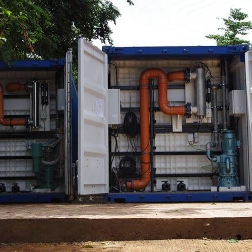 Interior of a BioKube BioContainer showing white polypropylene treatment tanks, orange blower pipework and pumps mounted inside the container