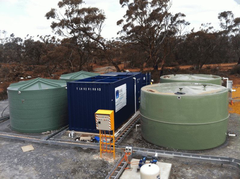 MAK Water containerized sewage treatment plant in a blue shipping container flanked by poly water tanks at a rural Australian site