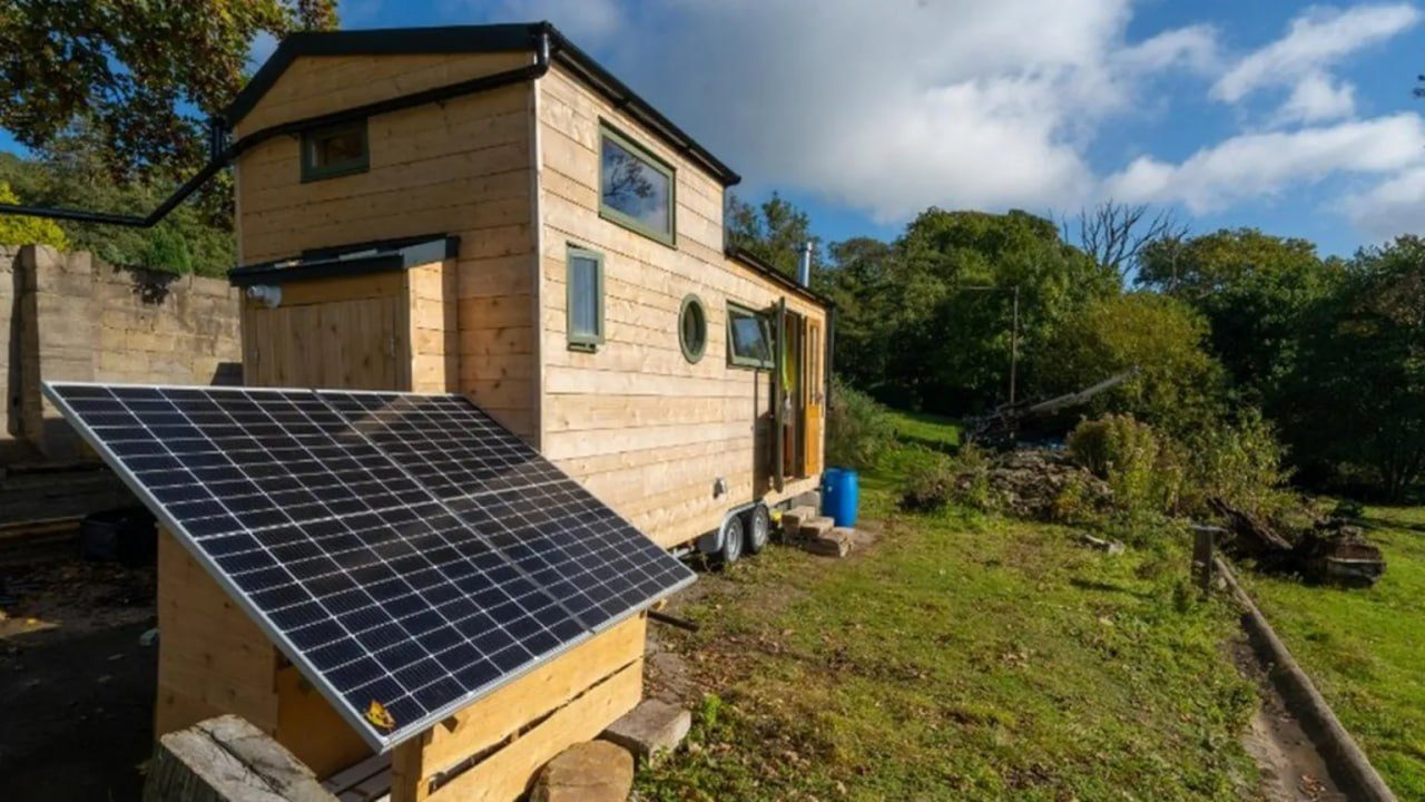 Solar panel on wooden frame beside a small timber cabin in a garden.