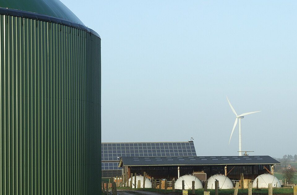 Farm with rooftop solar, wind turbine, and biogas digester domes.