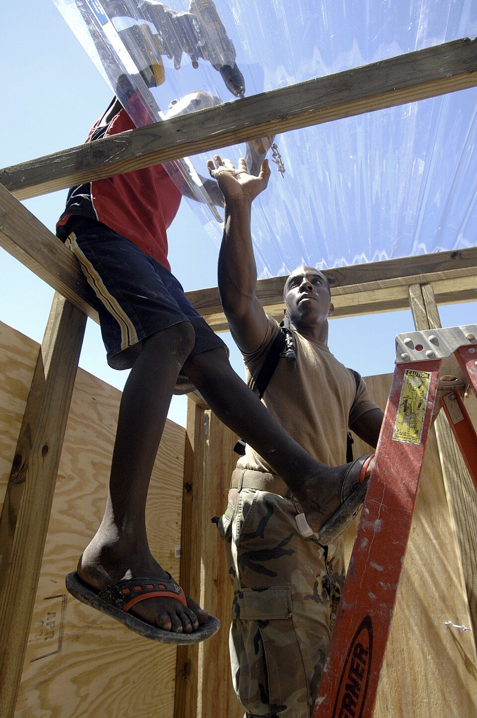 Two men assembling a wooden frame structure on a ladder.