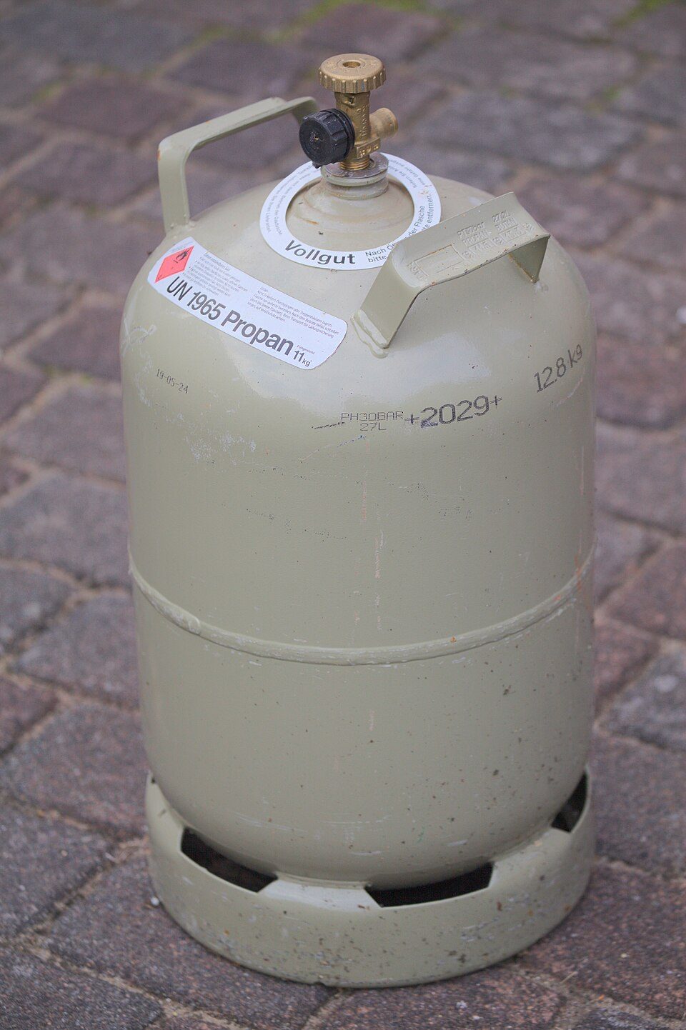 Beige propane cylinder with regulator valve on paved ground.