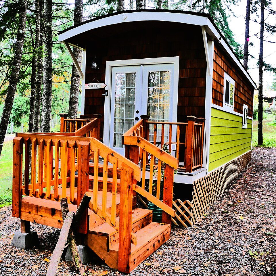 Small wooden tiny home with deck in woods.