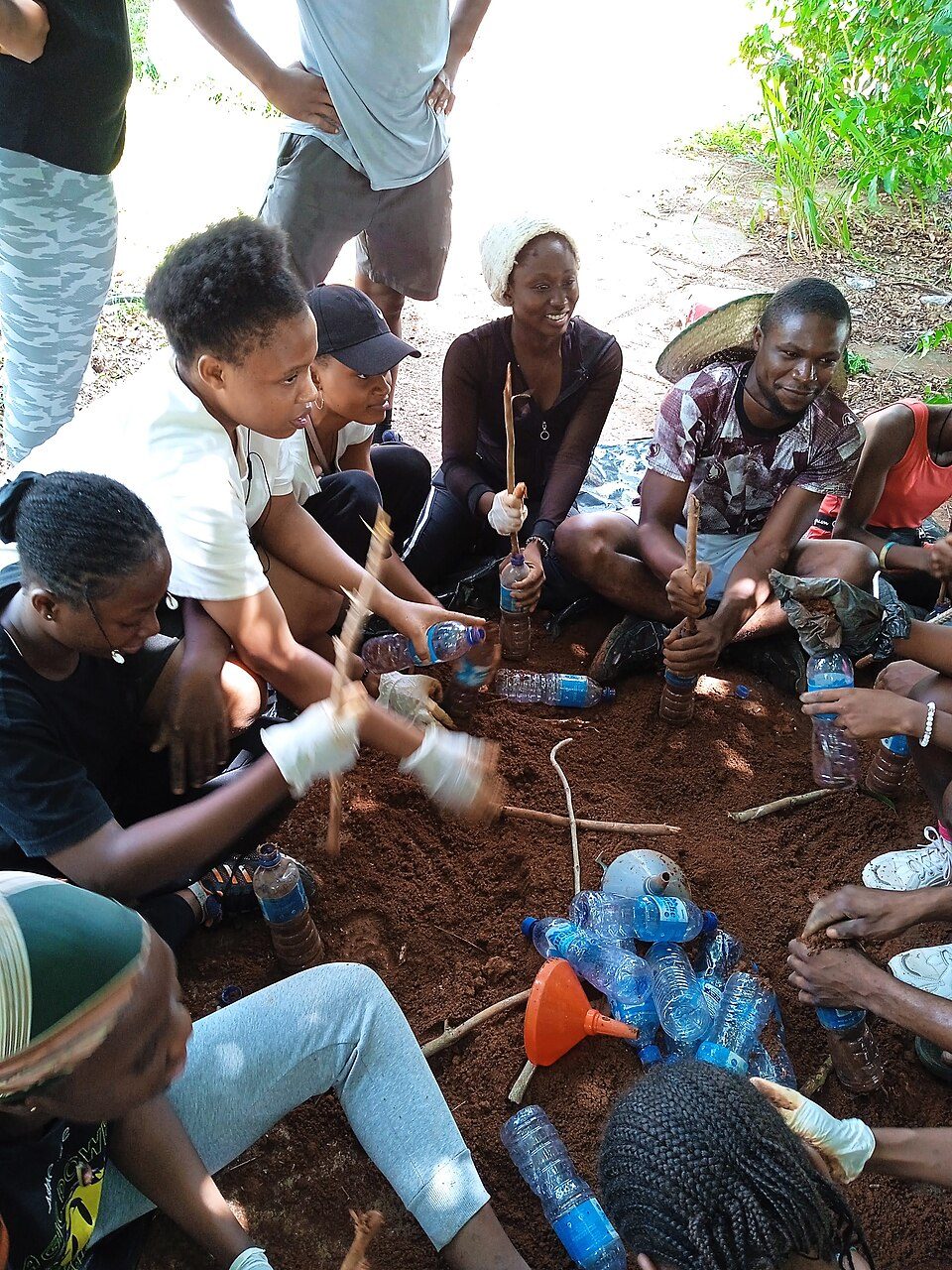 Group of people working with plastic bottles and sticks on the ground.